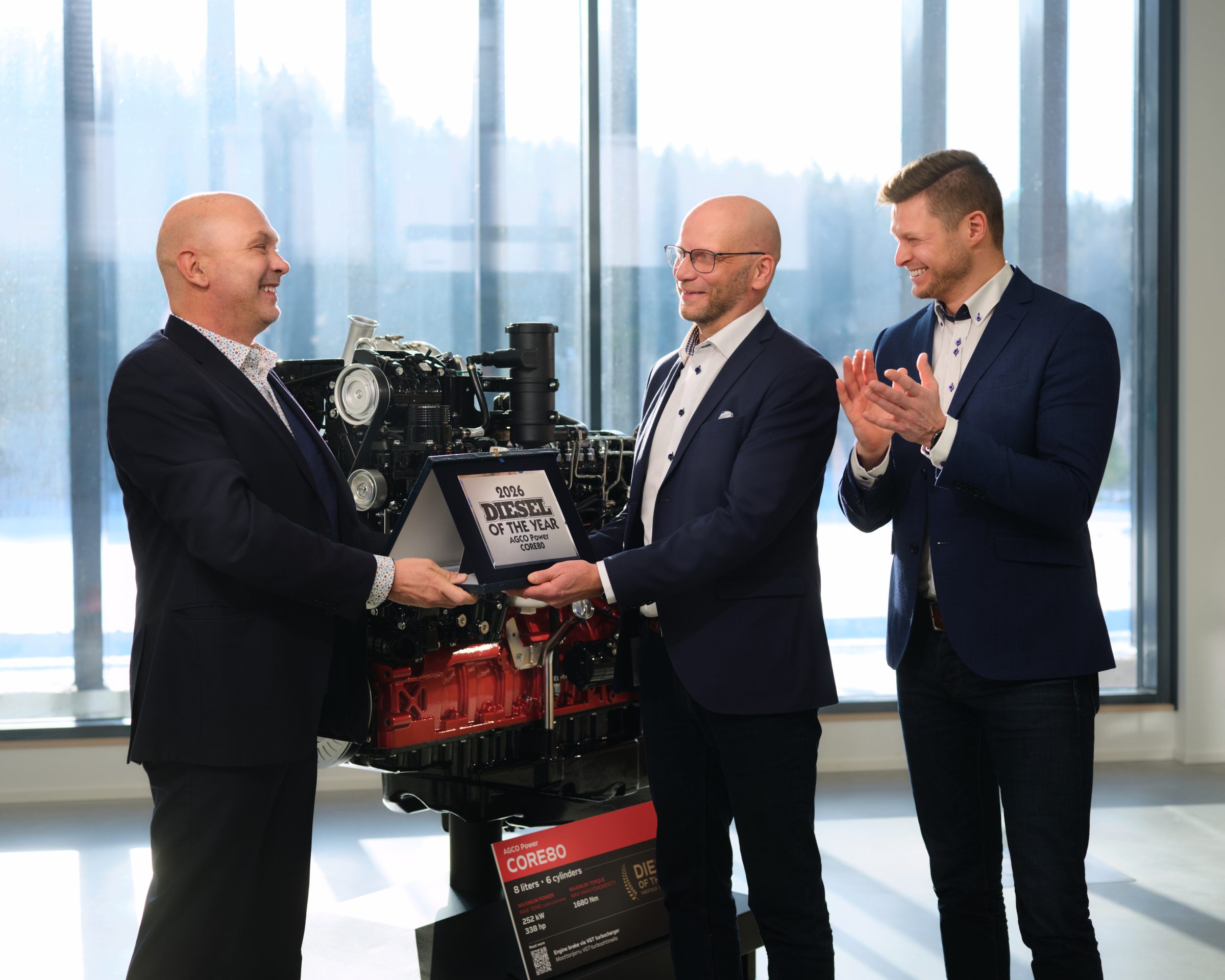 Powertrain International Editor‑in‑Chief Fabio Butturi (left) presents the Diesel Engine of the Year 2026 award to AGCO Power Vice President Juha Tervala. Next to them, AGCO Power Project Manager for Engineering Juha‑Pekka Asikainen applauds. In the background: the CORE80 engine.